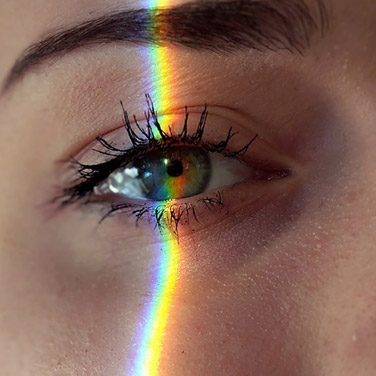 close up image of a woman's eye with a rainbow prism going through